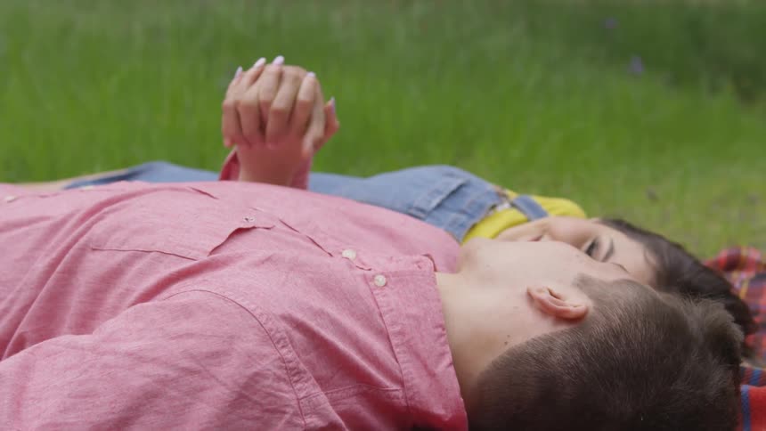 Lovers lay on towel in the grass and look at each other