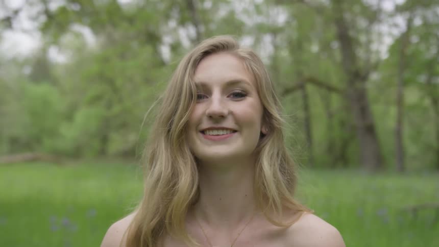 Young woman with makeup on face looks at and smiles in forest
