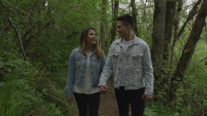 Man and woman walk along forest path holding hands