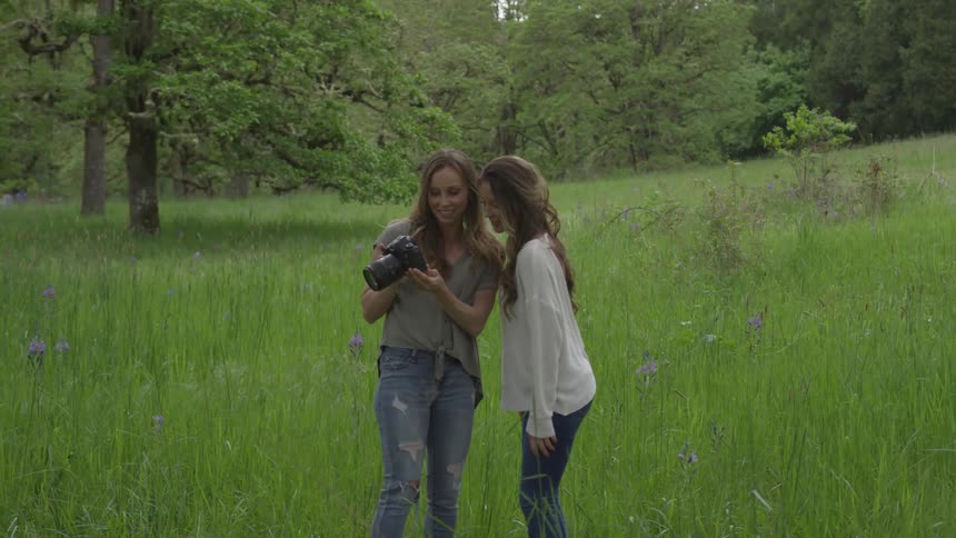 Two women stand in a field looking at a camera