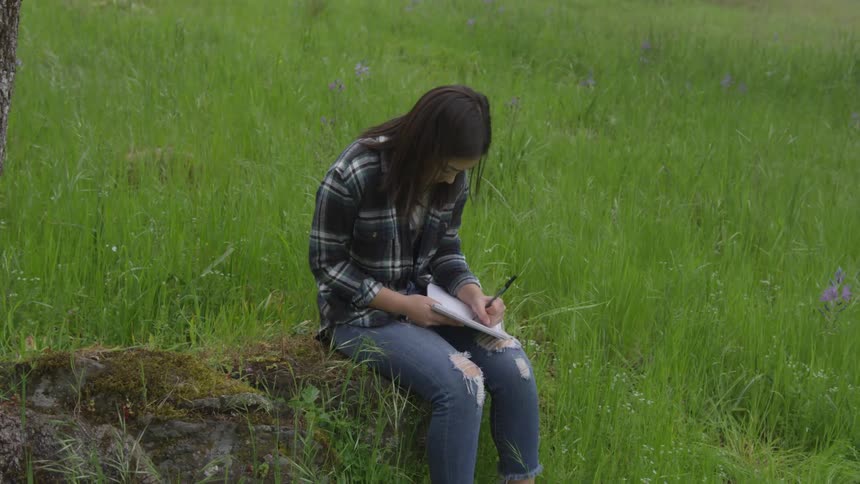 A woman sitting on a log writing on a notepad