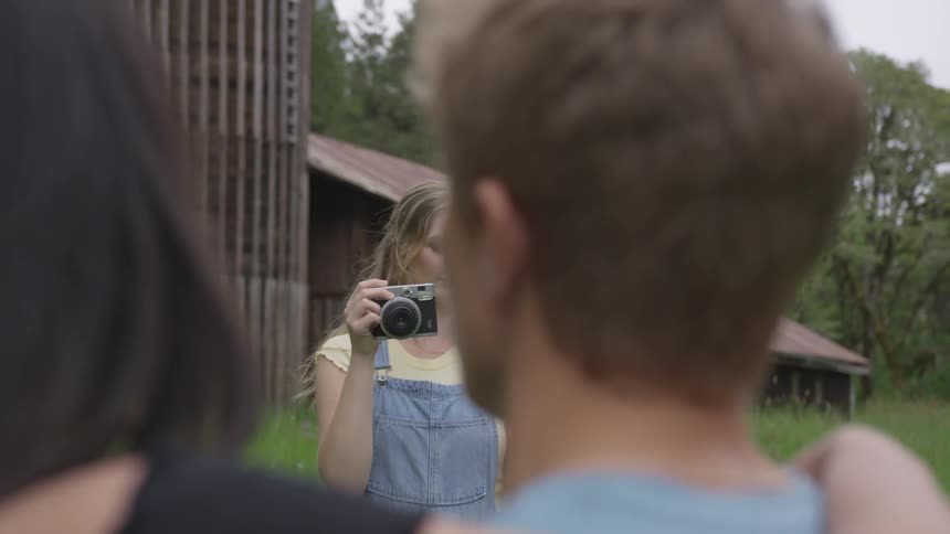 A woman takes a picture of a couple in a field