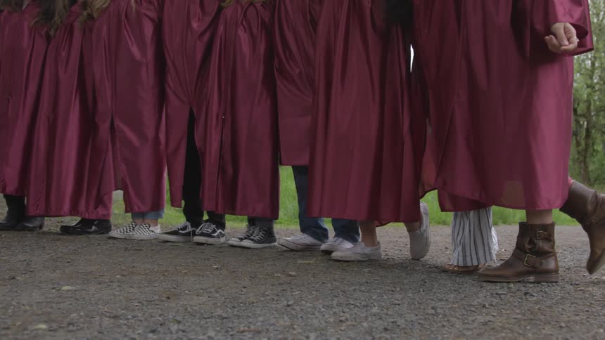 People are in graduation gowns outside in a wooded area