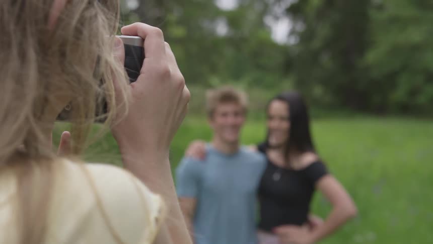 Woman takes photo of couple in front of grass