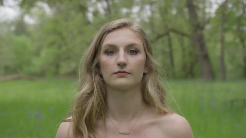 A blonde female wearing a necklace looks up from the ground