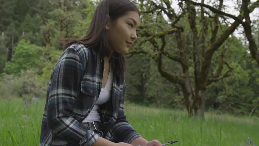A woman sitting in a field writing on a notepad