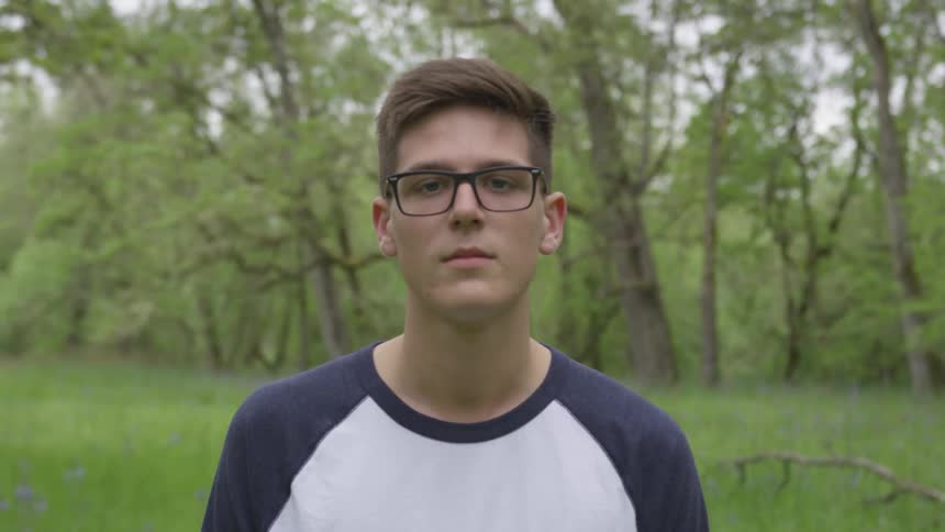 A man in glasses standing out in a field near the forest