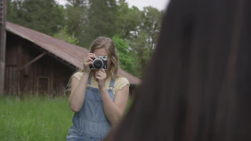 Woman is using camera with overgrown field and home in the background