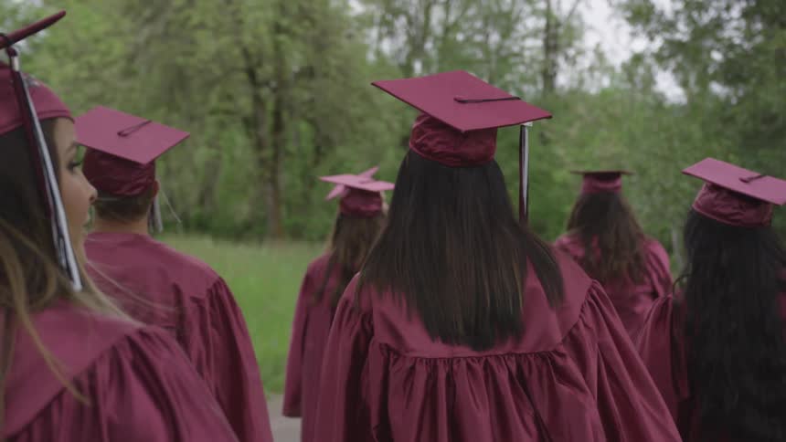 Group of students in cap and gown walks to a graduation ceremony