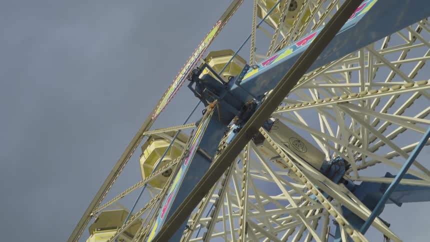 A ferris wheel painted yellow and blue rotates under a cloudy sky