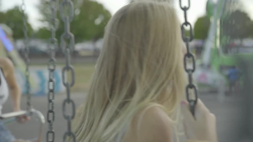 Girl swings while another girl leans on iron stick in amusement park at dusk