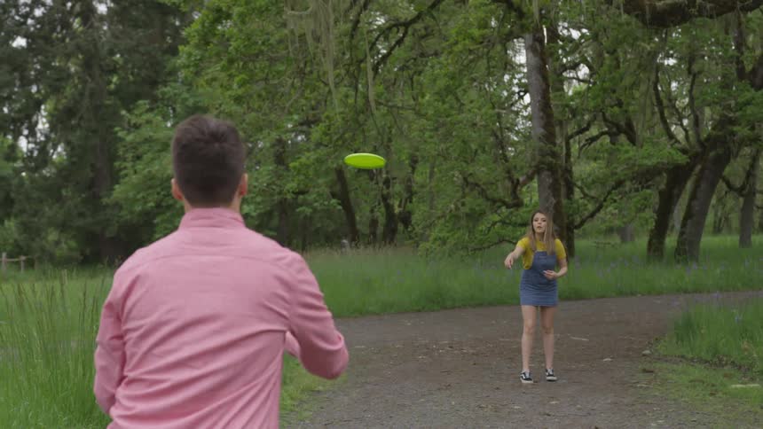 A couple is throwing a frisbee back and forth on a dirt road surrounded by tall grass and trees