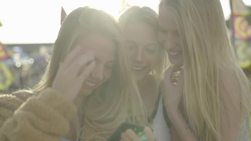 Three blonde girls look at cell phone and laugh