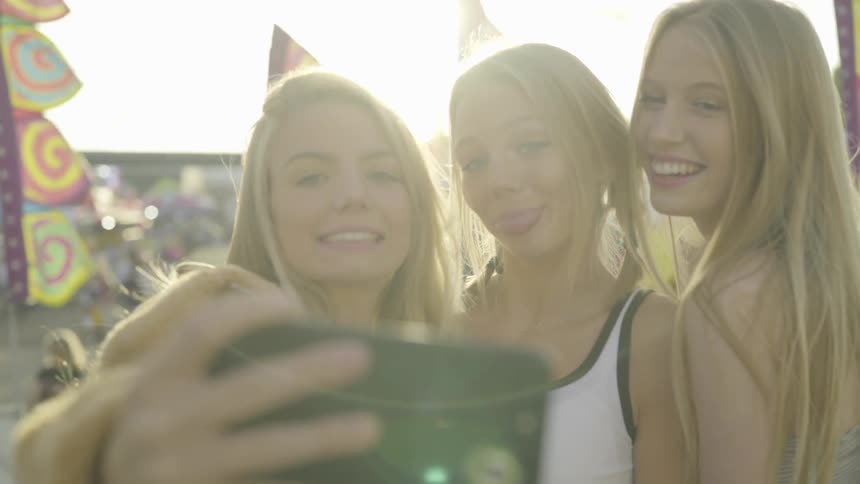 Three teenage girls taking selfies at a carnival