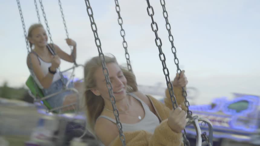 Two girls ride a fair swing with smiles on their faces