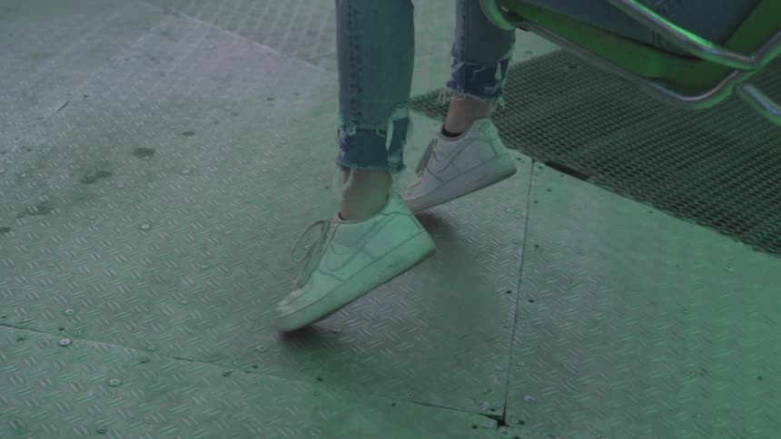 Girl who wears nike shoes sits on the swing by day