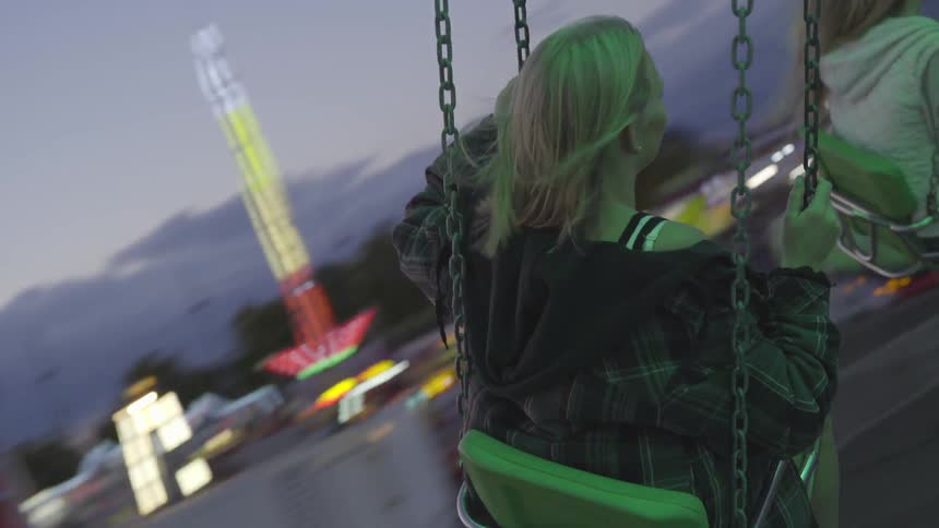 Blonde girl swings in the air in the amusement park at dusk