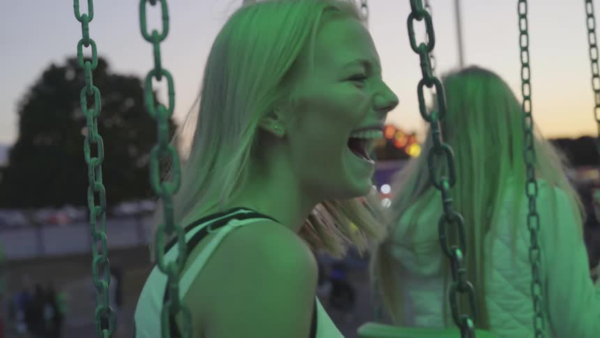 Woman sits on swing set laughing on fair grounds