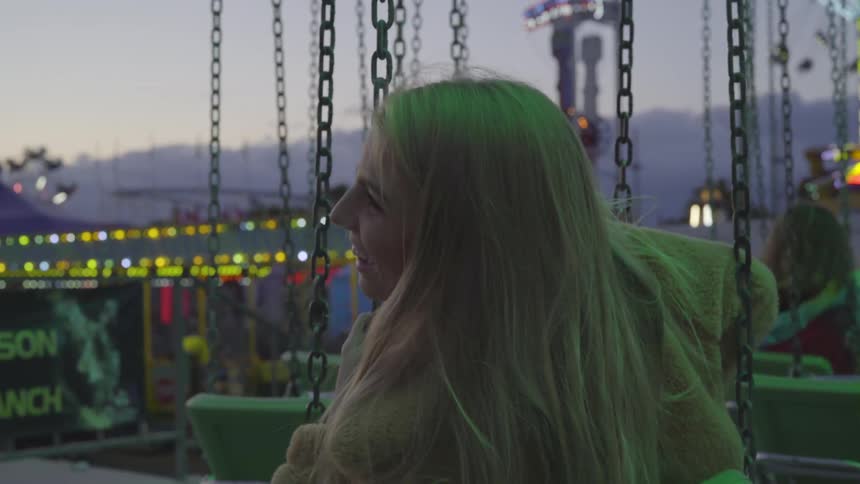 A woman sits on a swing suspended from chains at a fairground