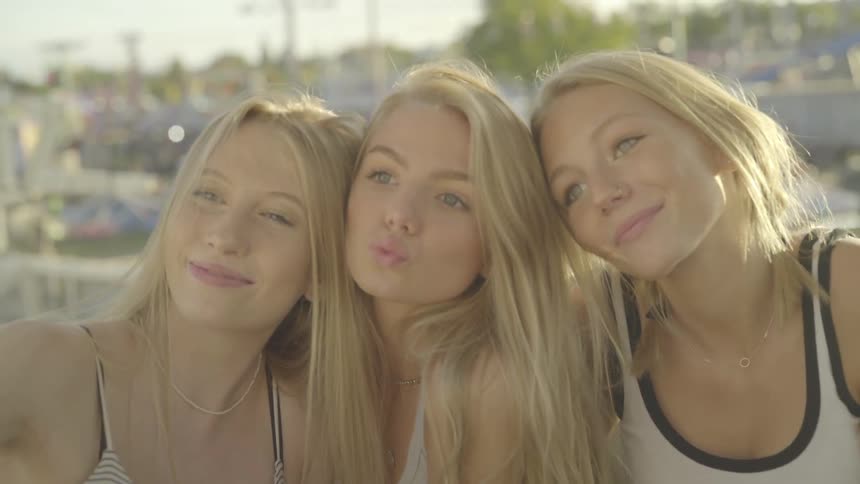 Three blond teenage friends smile and make faces for a selfie on a sunny day