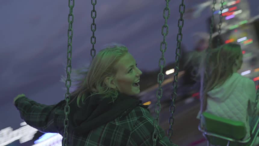 Blonde girl who has striped jacket swings in the air at dusk