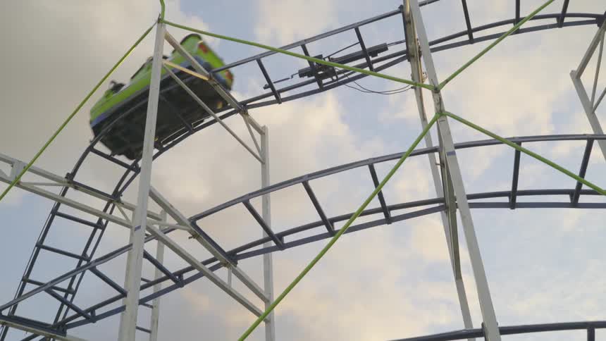 A roller coaster dips under a cloudy sky