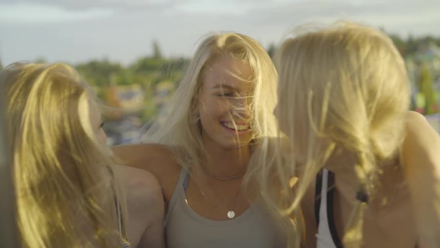 Three blonde women standing closely outside in the wind