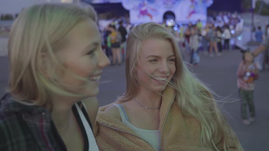 Girls laugh together at carnival with people and rides in the background