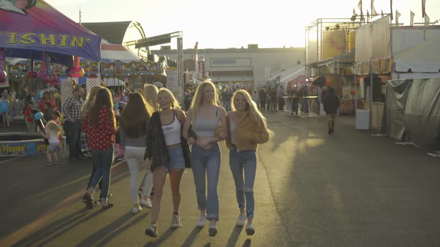 Three woman walking through a carnival surrounded by booths and people