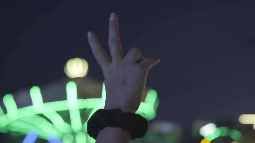 A person holding up two fingers at night at a carnival