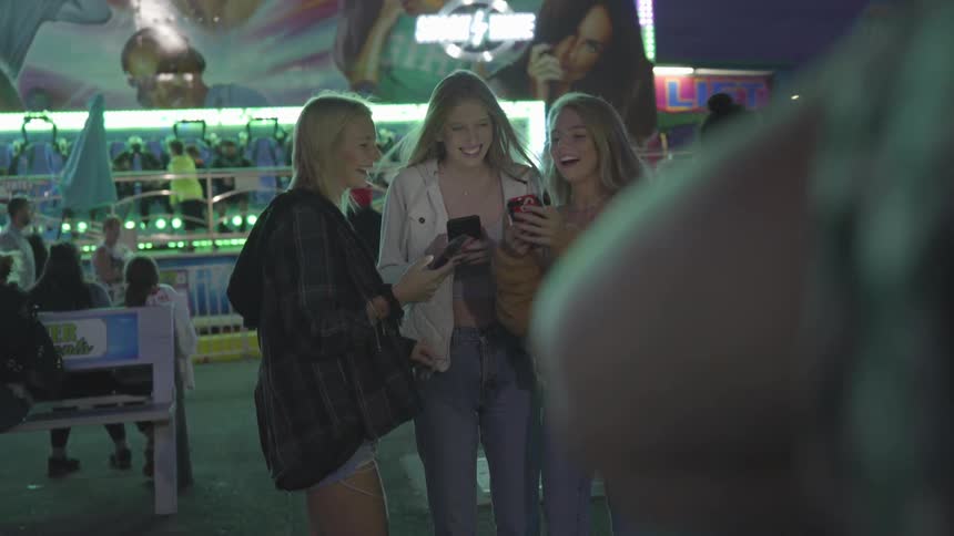 Girls laugh and show each other phones at carnival
