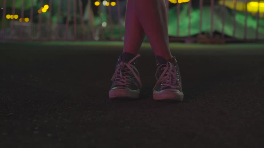 A person wearing converse shoes stands in front of a fairground
