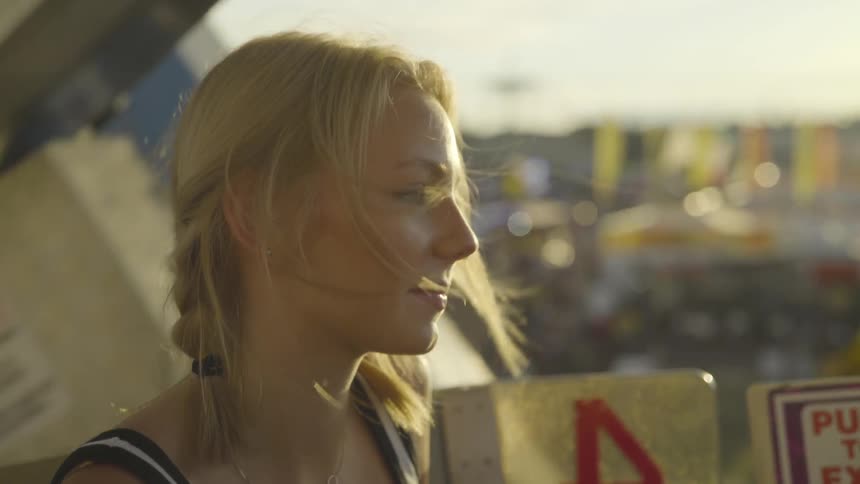 A young woman with blonde hair rides a ferris wheel at a carnival