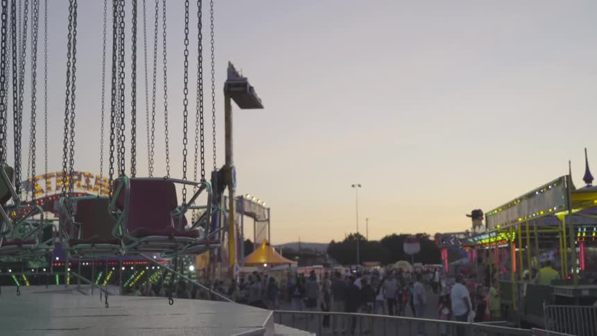 People walk past carnival rides and booth at sunset