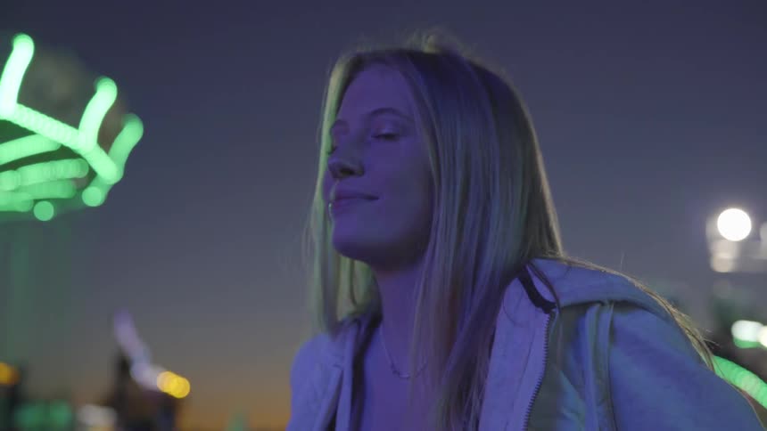Woman looks around in a brightly lit amusement park at night