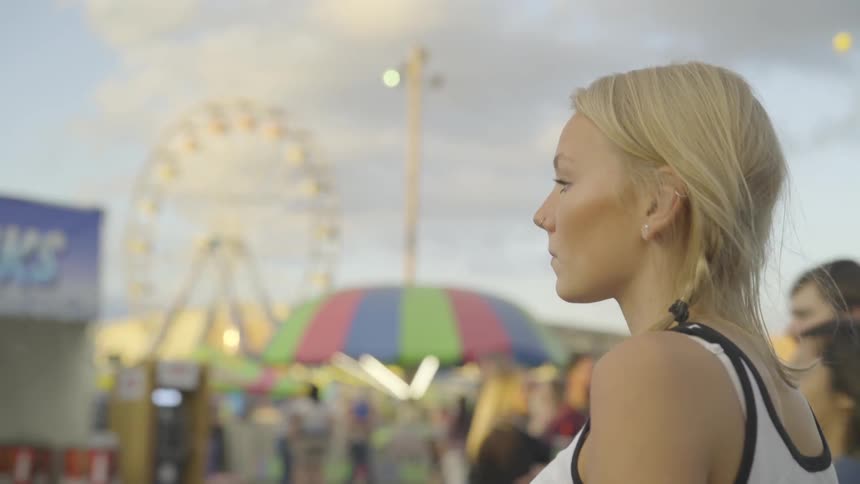 Blonde girl looks around in amusement park on a sunny day
