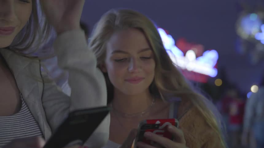 Two women are at a carnival looking at a cell phone