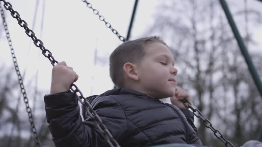 A small boy is swinging on a swing set outside