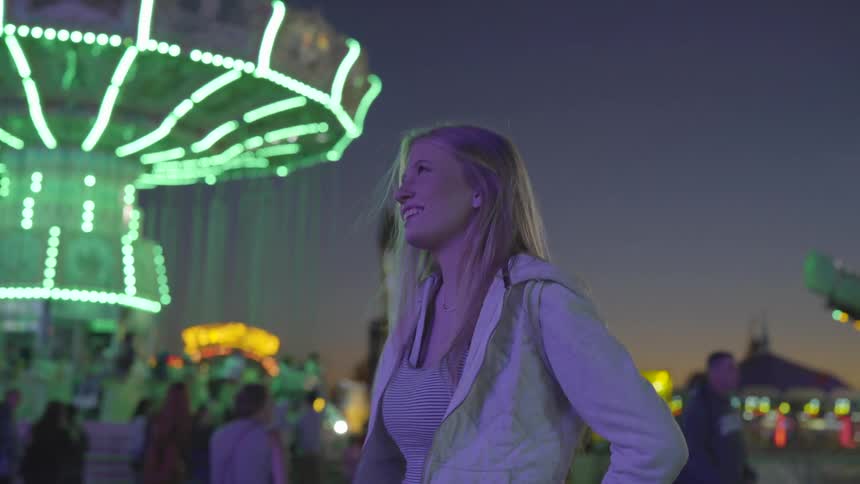 A woman in a jacket standing at a fair at night