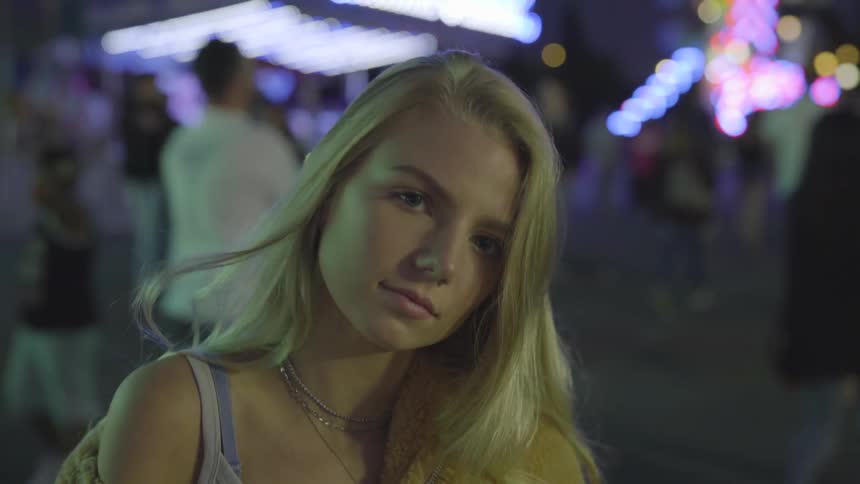 Girl touches her hair and smiles while posing by night
