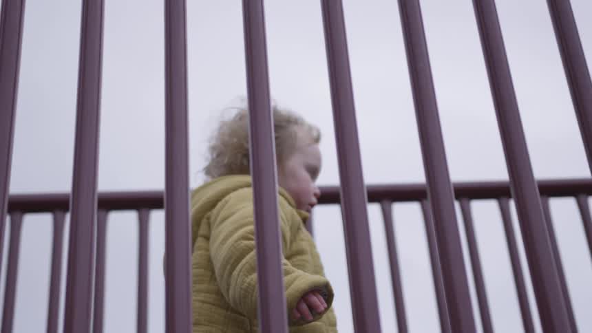 A toddler in a yellow coat walks on a playground toy