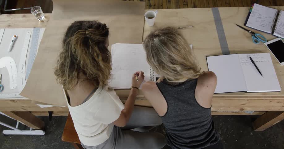 Two women reading note papers at a wooden table
