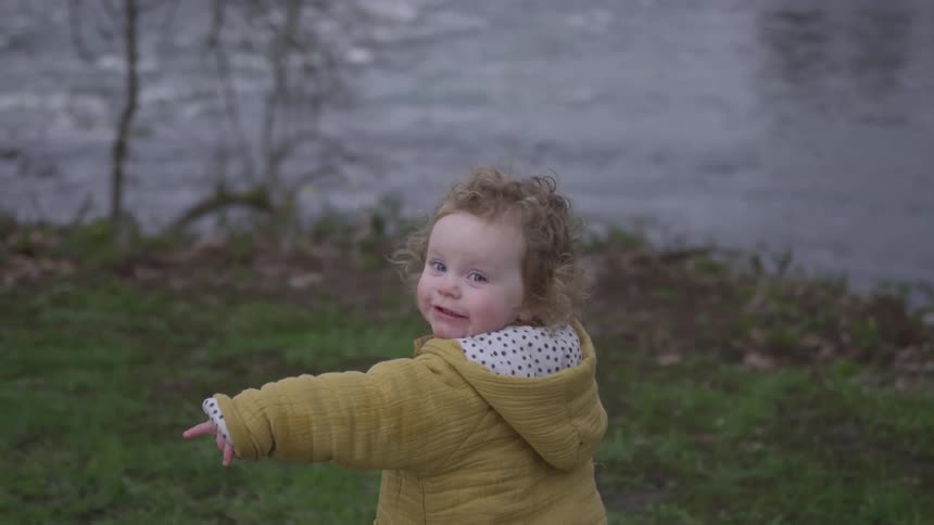 A toddler in a yellow coat points at something by a river
