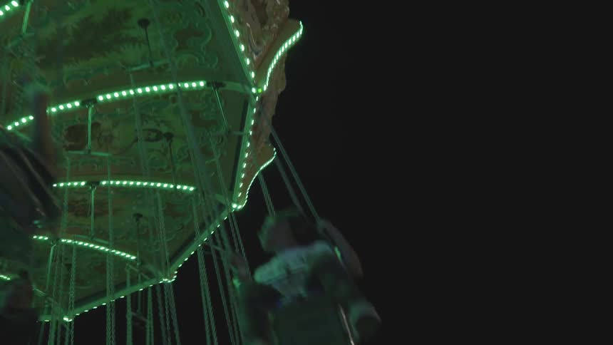 People fly by on a fair swing in the dark