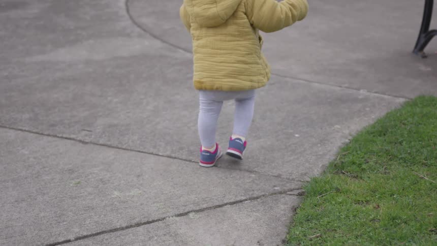 A toddler in a yellow coat runs to a bench