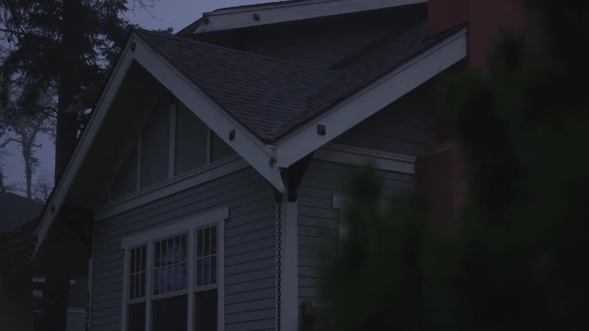 The large windows and roofline of a home become visible from behind a bush