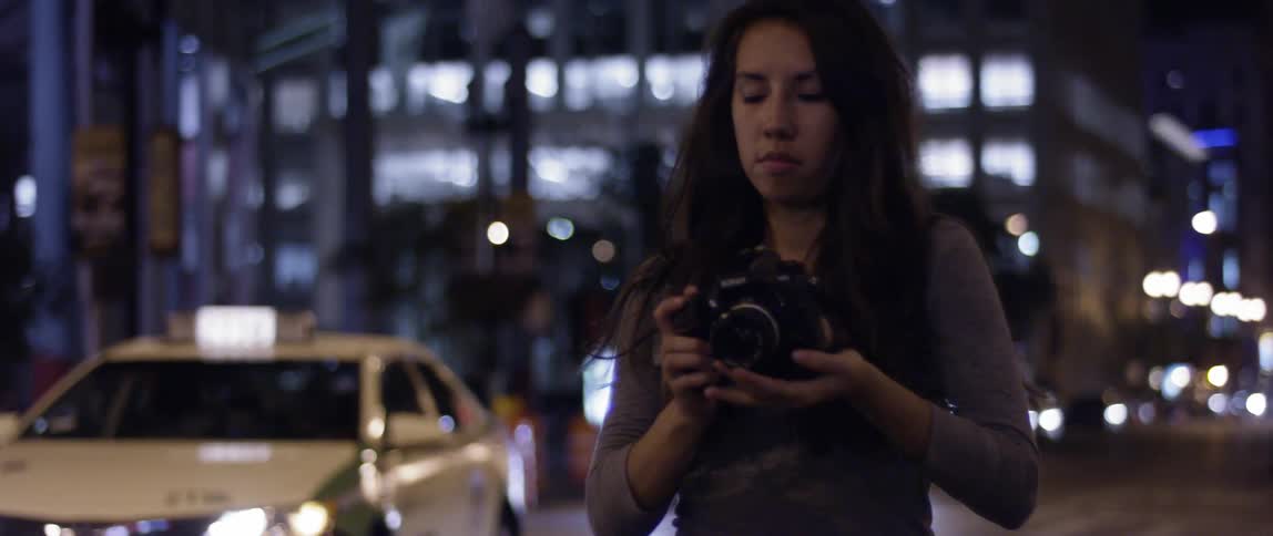 A woman is taking photographs in a city at night