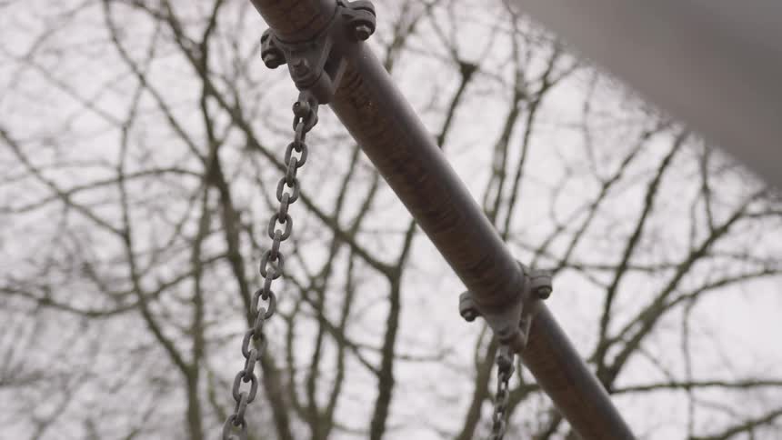 A chain swinging back and forth on a swing set in the woods