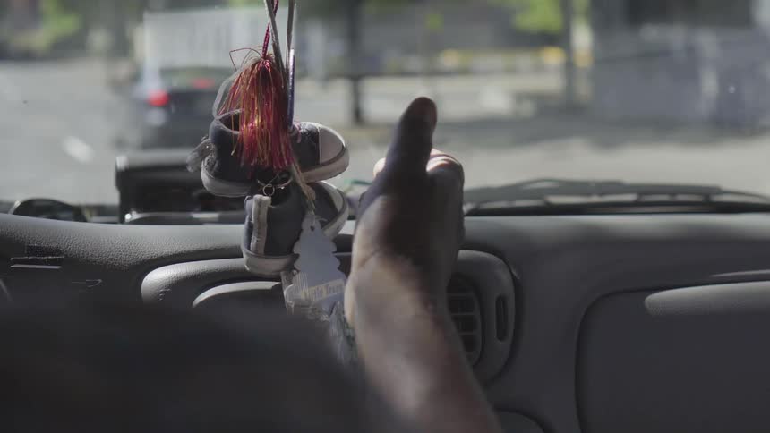 Car drives on a road and a person touches child's shoes hanging from rearview mirror