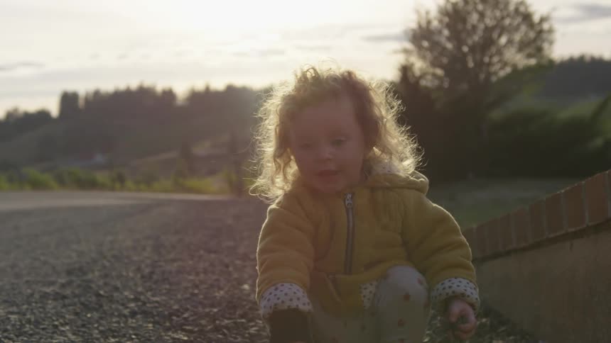 Toddler kneels and picks up rocks then throws them